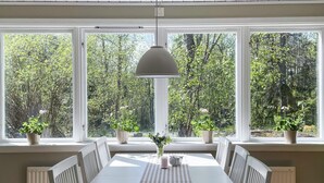 A dining area with a white table, chairs, and a hanging light fixture. There are potted plants on the windowsills and a radiator on the wall. - 4 Star Holiday Home in Vato (Vätö)