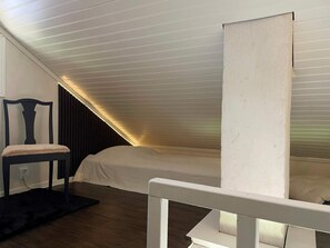 A room with a sloped ceiling, a bed, a chair, and a dark floor. - 4 Star Holiday Home in Vato (Vätö)