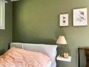A bedroom with a bed, a bedside lamp, and two framed botanical prints on the wall.