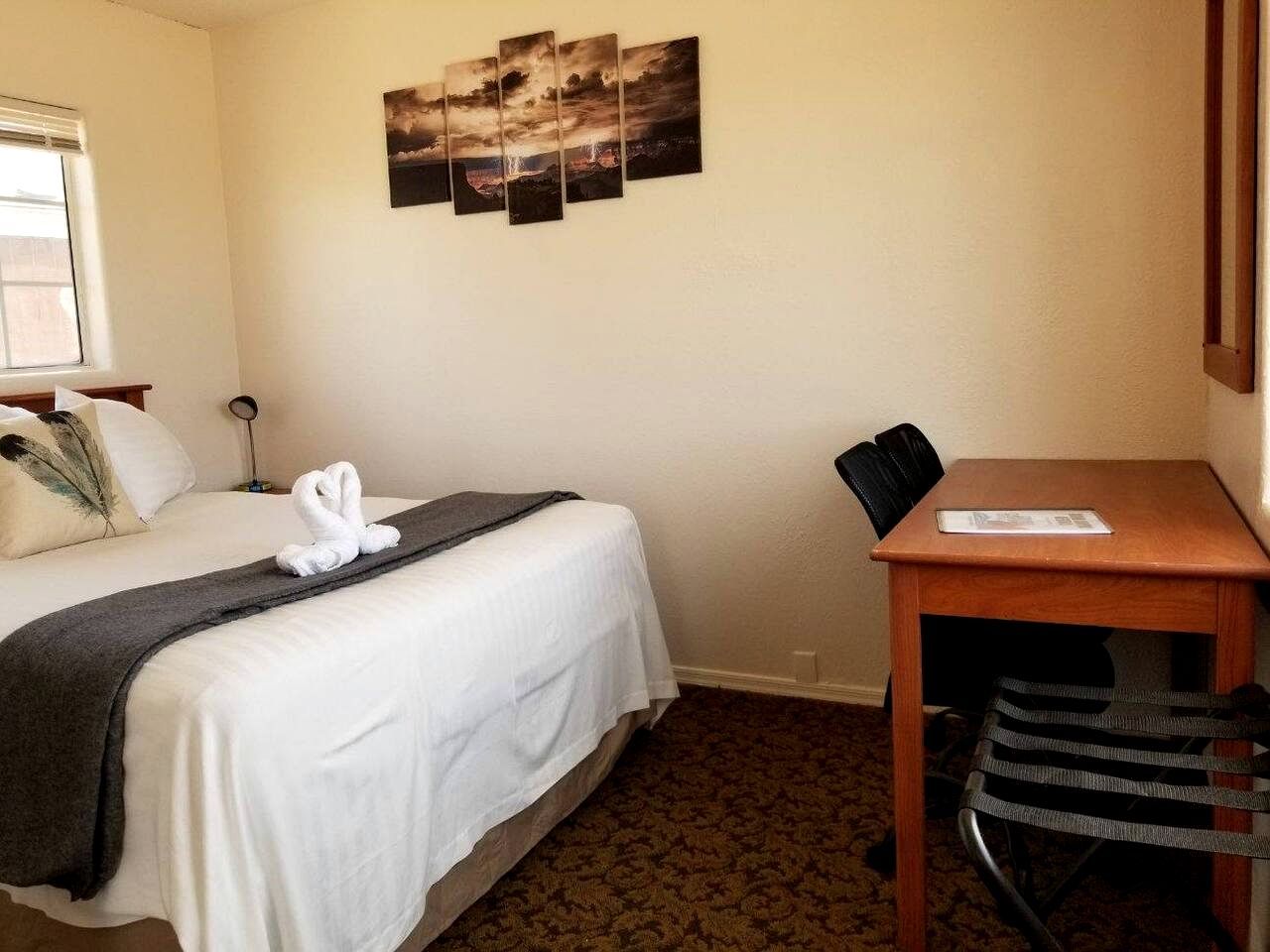 Ett hotellrum med en säng, ett skrivbord, en stol och ett konstverk som hänger på väggen.
