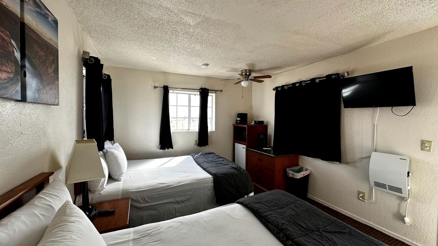 A hotel room with two beds, a ceiling fan, a TV, and a window with curtains.