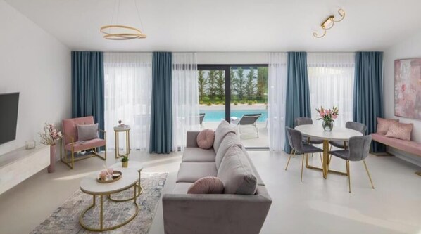 Ein modernes Wohnzimmer mit Sofa, Esstisch und Blick auf einen Pool.
