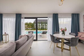 Ein modernes Wohnzimmer mit Blick auf einen Pool, einem runden Tisch mit Stühlen und einem Sofa.