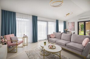 Ein modernes Wohnzimmer mit Sofa, Sessel, Couchtisch und Vorhängen.