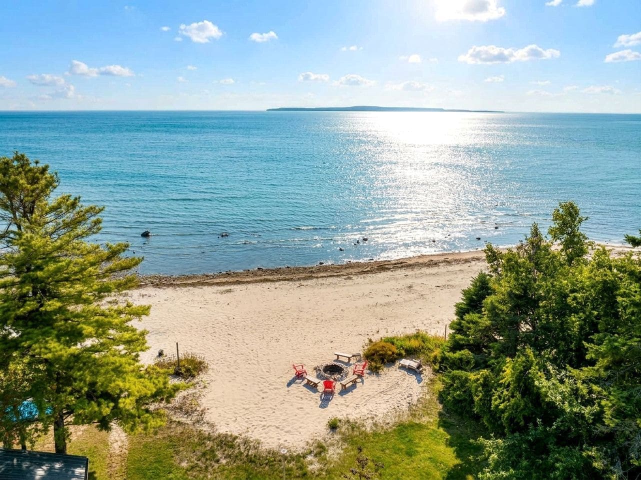 Une plage avec un foyer et des chaises, entourée d’arbres et offrant une vue sur la mer.