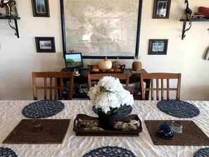 Una mesa de comedor con mantel blanco, un jarrón de flores blancas y una computadora portátil.