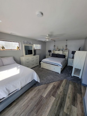 Een slaapkamer met een bed, een kaptafel, een nachtkastje, een plafondventilator en een raam.