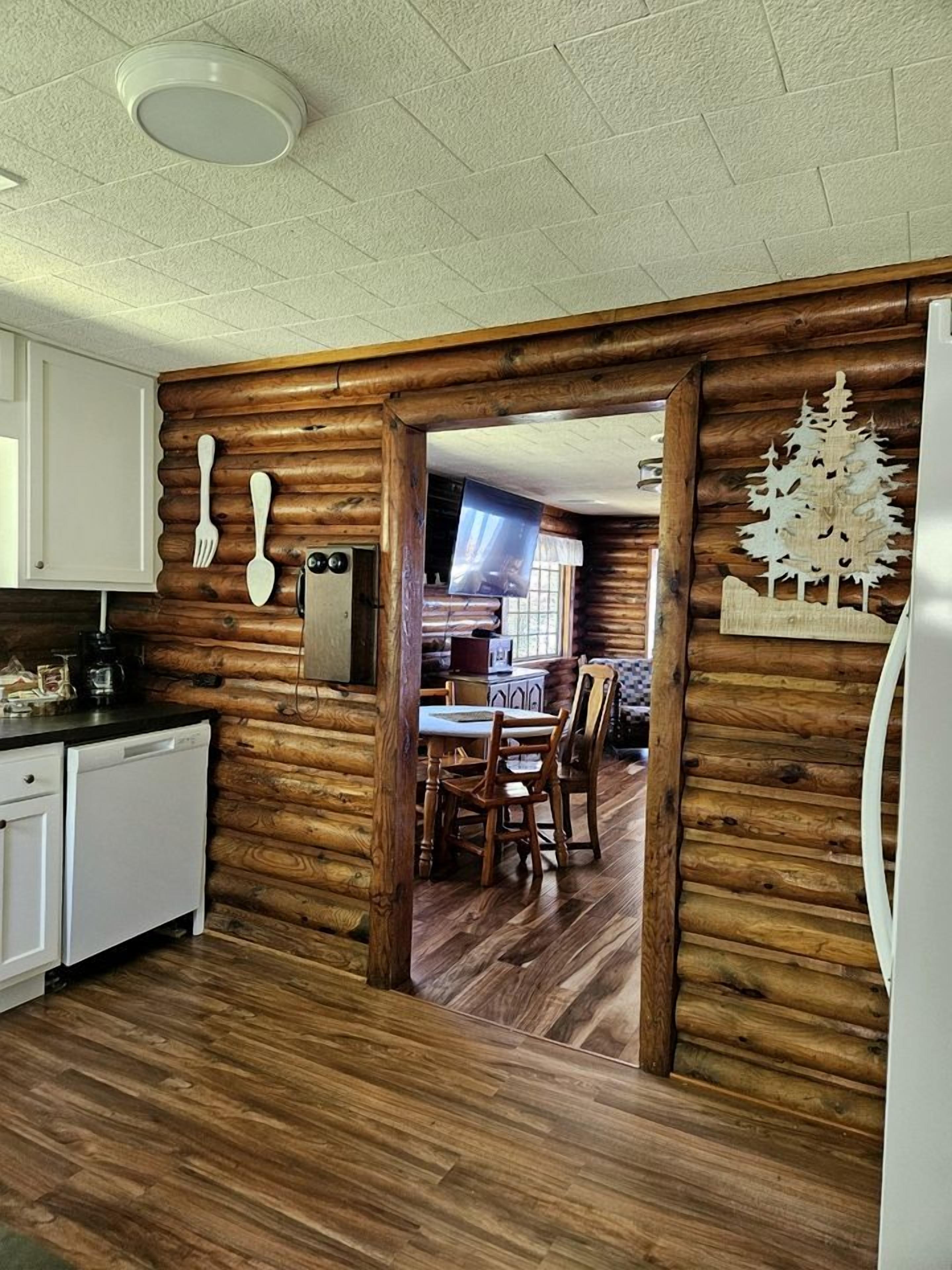 A log cabin interior with a kitchen, dining area, and a wooden wall with a tree decoration.