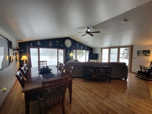 A dining area with a wooden table and chairs, a sofa, and a television. - Fantastic Lakefront Beach House with Stunning Views in St. Ignace, Michigan (St. Ignace)