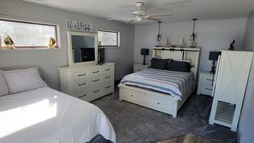Une chambre à coucher comprenant un lit, une commode, une table de chevet, un ventilateur de plafond et une fenêtre.