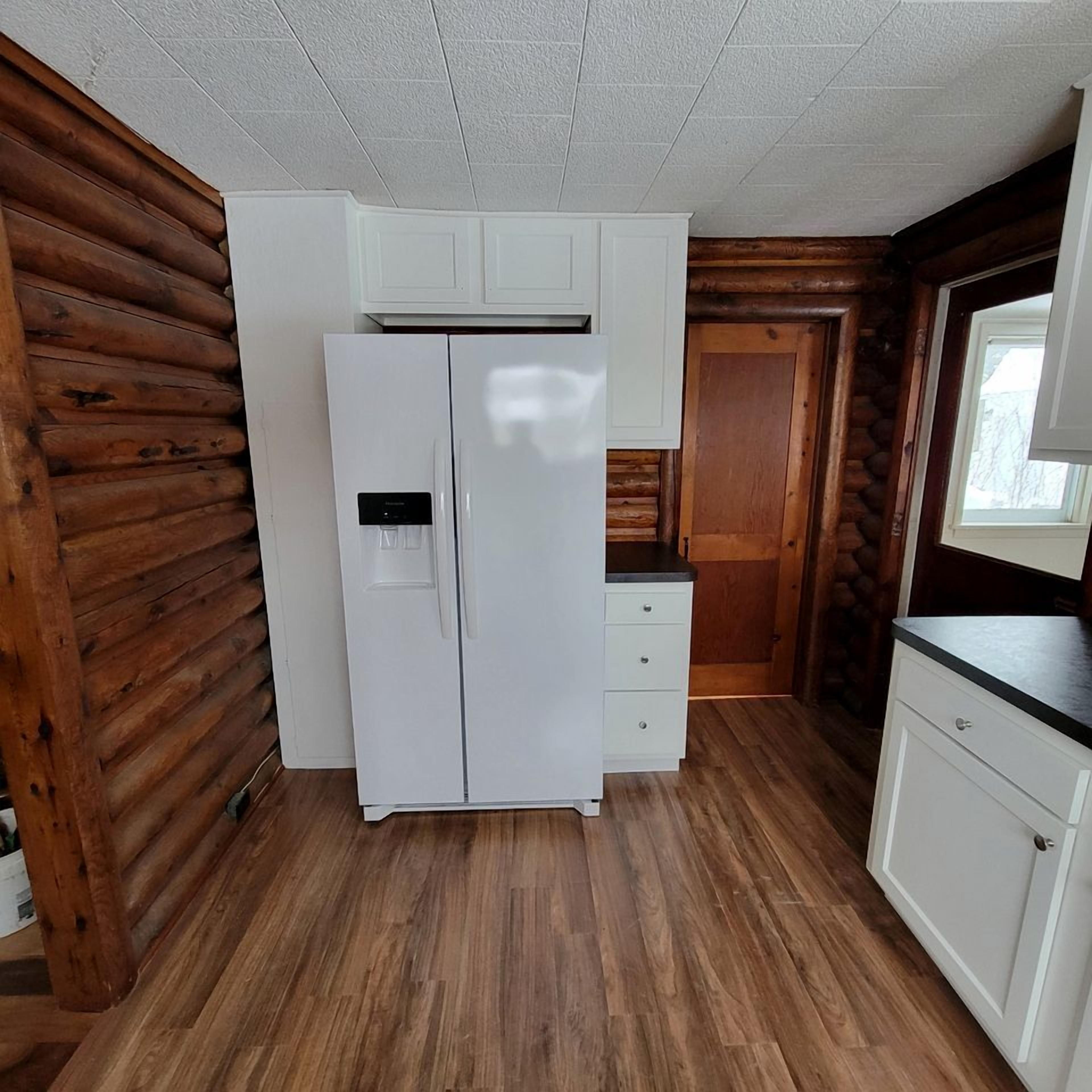 Une cuisine de taille réduite avec un réfrigérateur blanc, des armoires en bois et un mur en pierre.