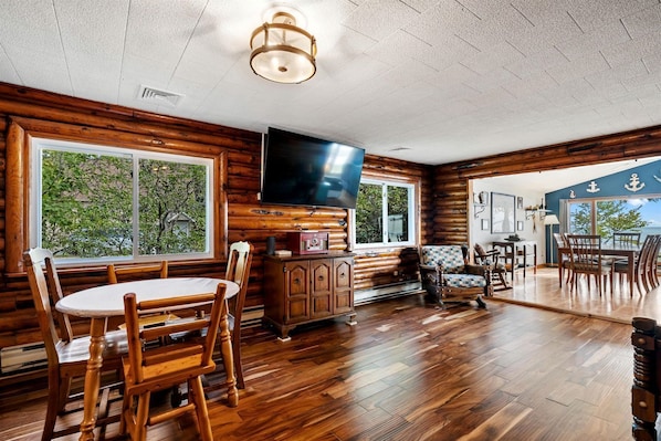 A log cabin interior with a dining area, a kitchen, and a large window offering a view of the outdoors. - Fantastic Lakefront Beach House with Stunning Views in St. Ignace, Michigan (St. Ignace)