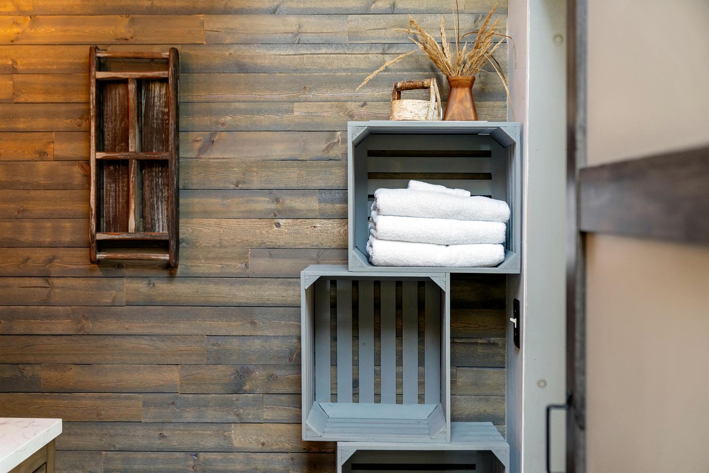 Een houten wand met een rustieke plankenwand, waarin gevouwen handdoeken en een decoratieve vaas staan.
