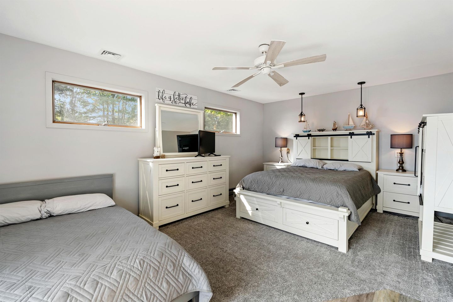 A bedroom with a bed, dresser, vanity, and a ceiling fan.