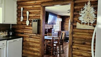 A log cabin interior with a kitchen, dining area, and a wooden wall with a tree decoration.