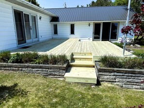 A house with a wooden deck, a stone retaining wall, and a metal roof. - Fantastic Lakefront Beach House with Stunning Views in St. Ignace, Michigan (St. Ignace)