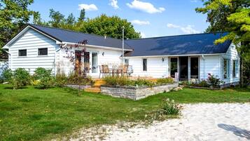 Ein zweigeschossiges Haus mit einer Veranda, einer Steinmauer und einem Rasen.