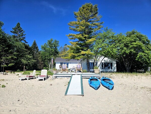 A beach house with a dock, two paddle boats, and beach chairs.