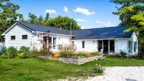 A two-story house with a covered porch, a stone retaining wall, and a grassy yard. - Fantastic Lakefront Beach House with Stunning Views in St. Ignace, Michigan (St. Ignace)