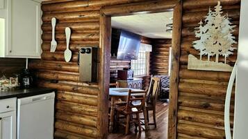 A log cabin interior with a kitchen, dining area, and a wooden wall with a tree decoration.