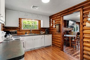 Interior de una cabaña de troncos con cocina, comedor y sala de estar visible.