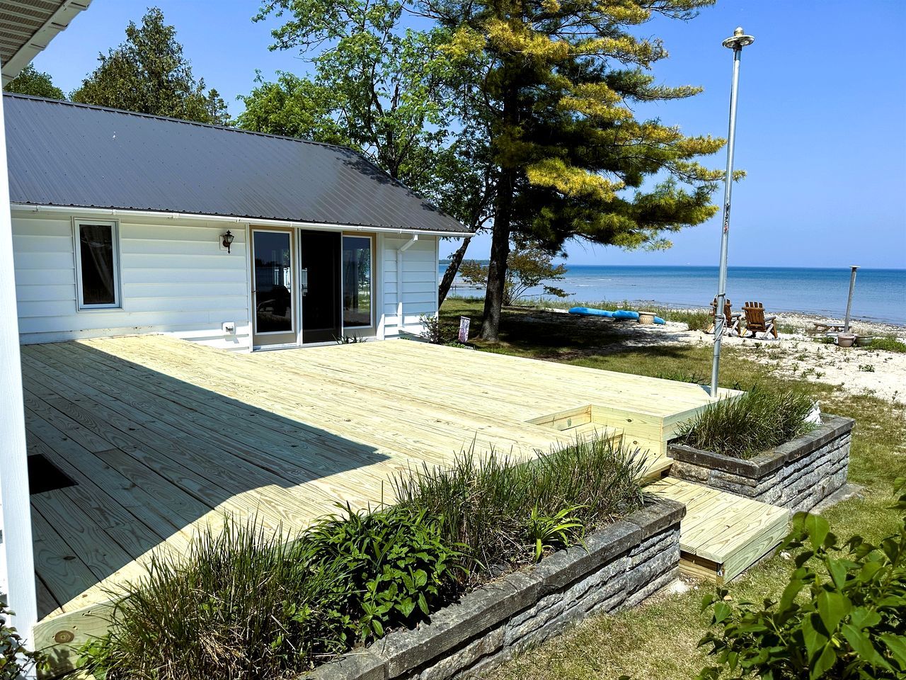 A house with a wooden deck, a glass door, and a view of the beach.