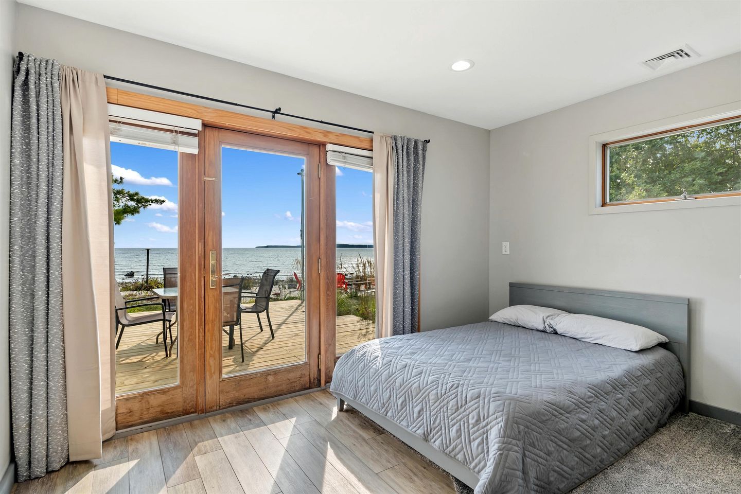 A bedroom with a bed, a view of the sea through a sliding door, and a wooden deck outside.