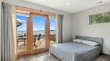 A bedroom with a bed, a view of the sea through a sliding door, and a wooden deck outside.