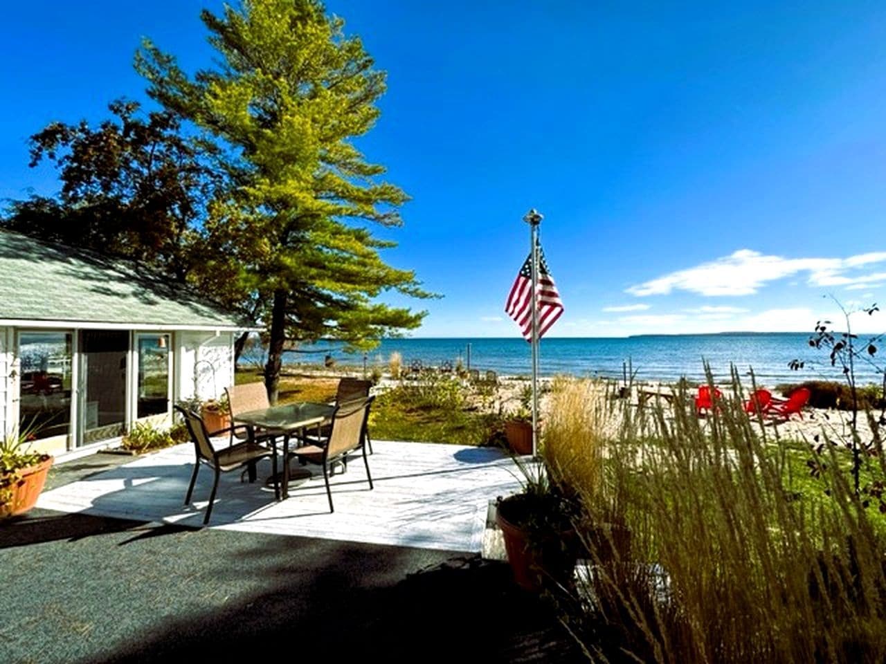 A patio with a table and chairs, an American flag, and a view of the beach.