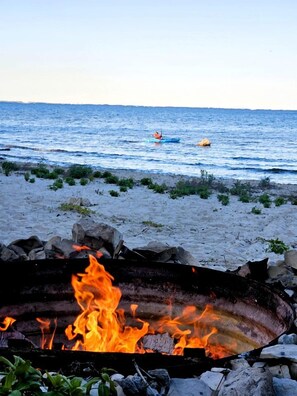 Una playa con un hogar para fuego al frente y una persona remando en kayak en el agua.