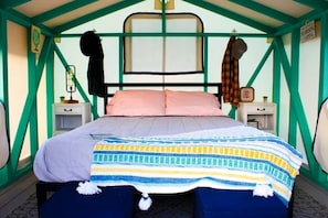 Un lit avec une couverture à rayures, deux oreillers et une tête de lit. Il y a deux tables de chevet avec des lampes et une horloge.