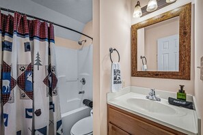 Ein Badezimmer mit Duschvorhang, Toilette, Waschbecken mit Spiegel und Handtuchhalter.