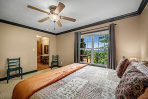 Un dormitorio con una cama, un ventilador de techo, una ventana con vistas y dos sillas.