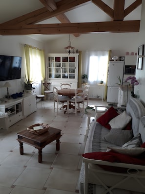 A living room with a sofa, coffee table, TV, and dining area with chairs and a cabinet.