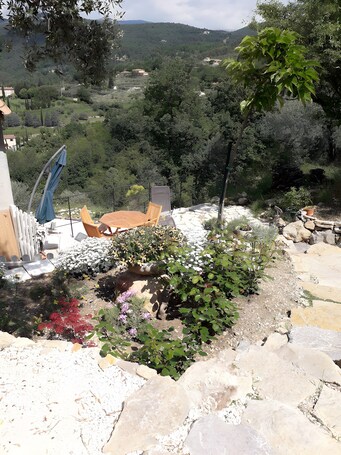 Une terrasse avec des meubles d’extérieur, un chemin de pierres et un jardin agrémenté de différentes plantes.. Chambre d’hôtes « Charmante chambre double dans villa » avec vue montagne, Wi-Fi, climatisation
