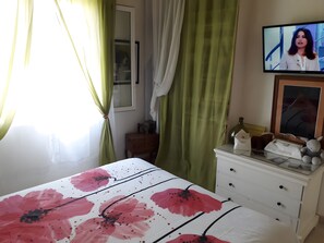 Ett sovrum med en säng, en byrå, en tv och ett fönster med gardiner.