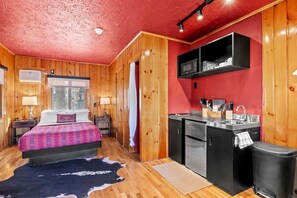 Ein Zimmer mit einem Bett, einer kleinen Küchenzeile und einem Fenster.