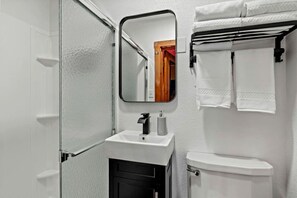 Et badeværelse med en hvid vask, et spejl, et toilet og en håndklædestang.