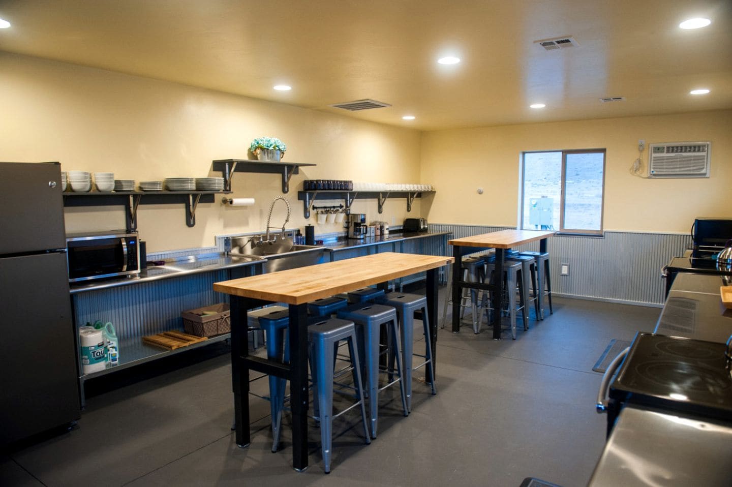 Una cocina con una mesa de madera, taburetes de bar azules, un microondas y un refrigerador.