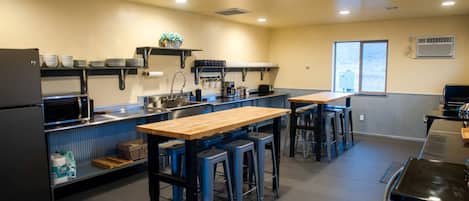 Una cocina con una mesa de madera, taburetes de bar azules, un microondas y un refrigerador.
