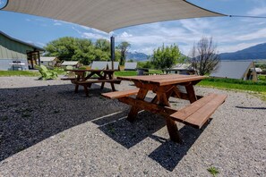 Piknicktafels buiten, beschaduwd door een overkapping, met een grindpad en gebouwen op de achtergrond.