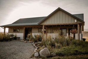 A two-story building with a porch, large windows, and a gravel driveway. - Charming A-Frame Cabins with Shared Kitchen, BBQ & Mountain Views in Emigrant, Montana (Emigrant)