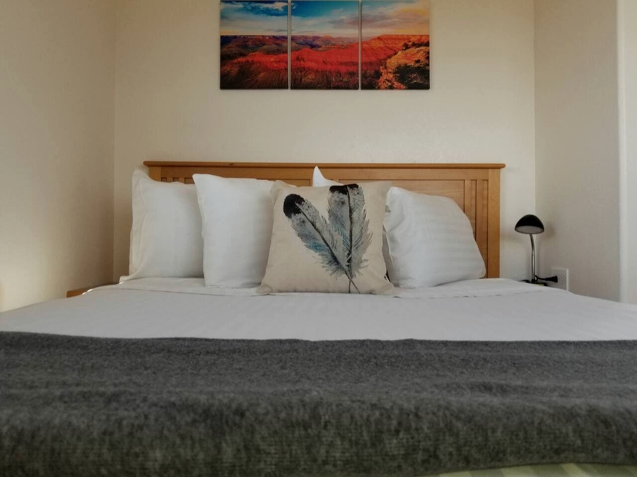 A bed with white bedding, a feather pillow, and a landscape painting above it.