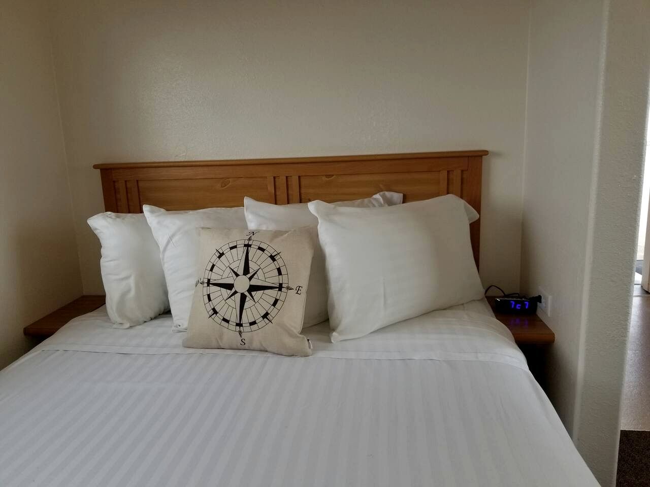 A bed with a wooden headboard, white bedding, and a compass-themed pillow.