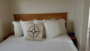 A bed with a wooden headboard, white bedding, and a compass-themed pillow.