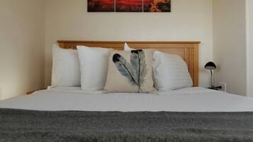Una cama con ropa de cama blanca, un almohadón de plumas y un cuadro de paisaje en la parte superior.