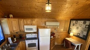 Interior de una cabaña de madera con kitchenette, un sofá de cuero marrón y una mesa de comedor.