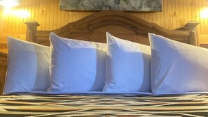 Una cama con almohadas blancas y una colcha estampada en una habitación con paredes de madera y un cuadro de un vaquero a caballo.