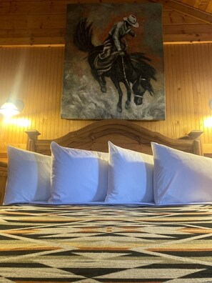 Een bed met witte kussens en een beddekleed met een patroon in een kamer met houten wanden en een schilderij van een cowboy te paard.