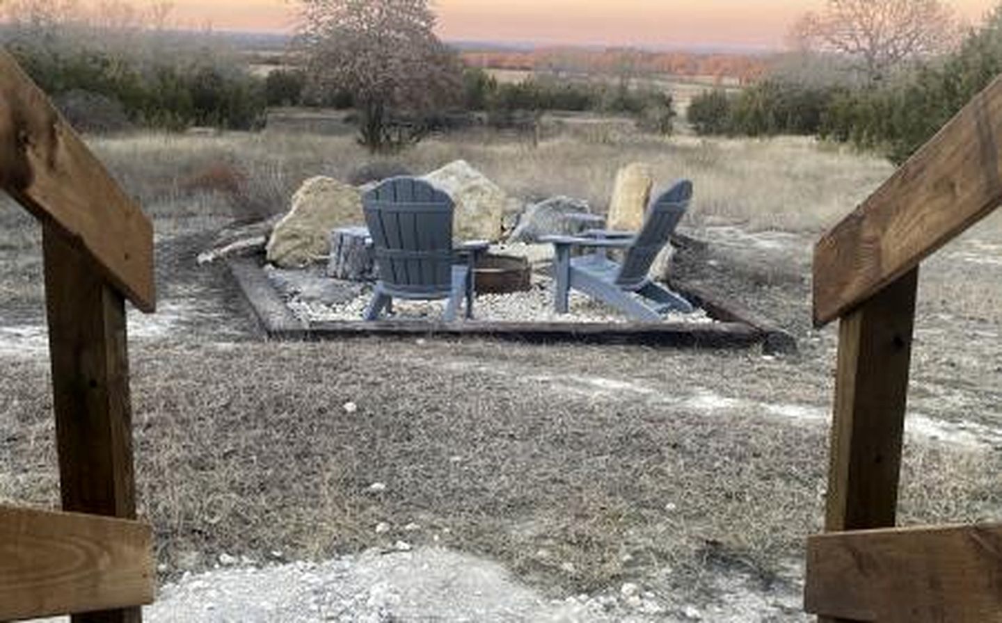 A wooden deck with two Adirondack chairs and a fire pit.